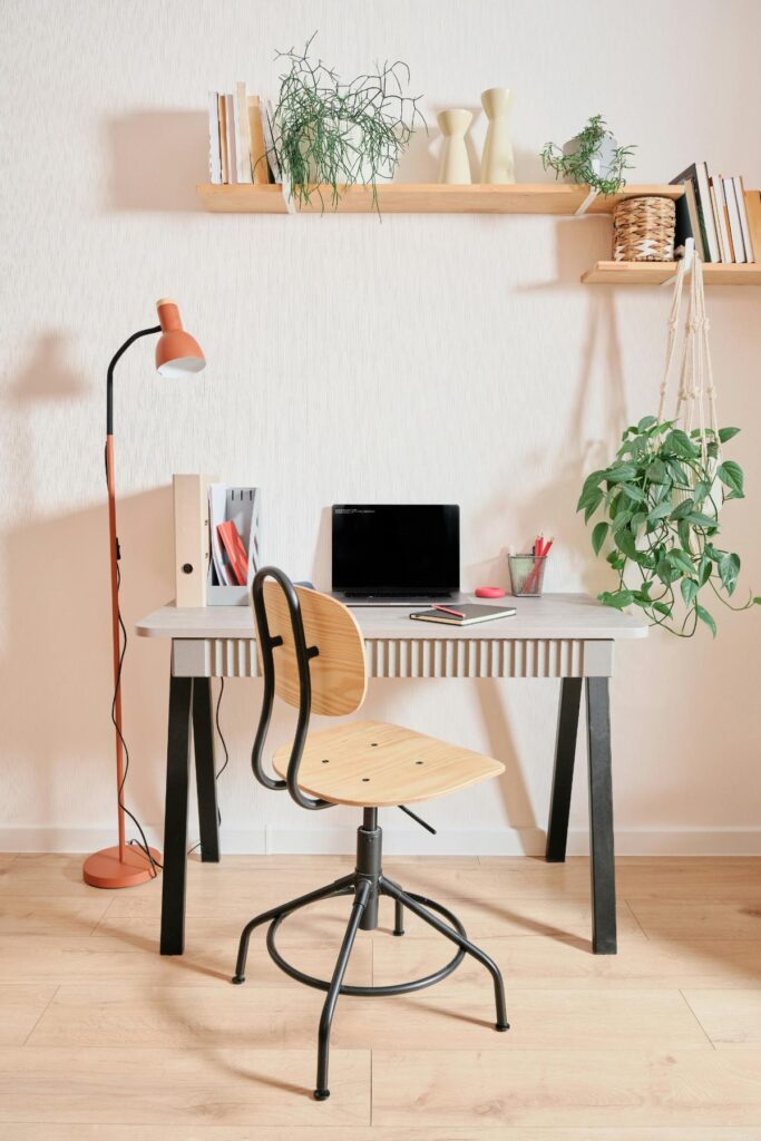 Stylish home workspace with a wooden chair, laptop, indoor plants, and shelves, reflecting the growing trend for aesthetically pleasing remote work areas.