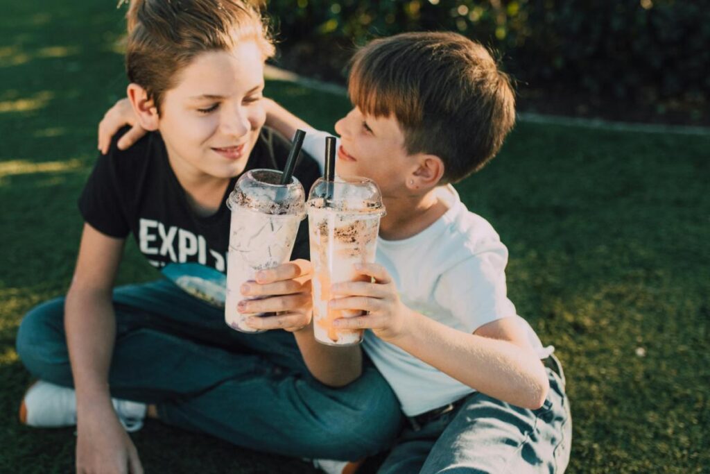 Kids enjoying chilled non-coffee drinks with whipped cream and chocolate, perfect for outdoor playdates and family café-style treats.