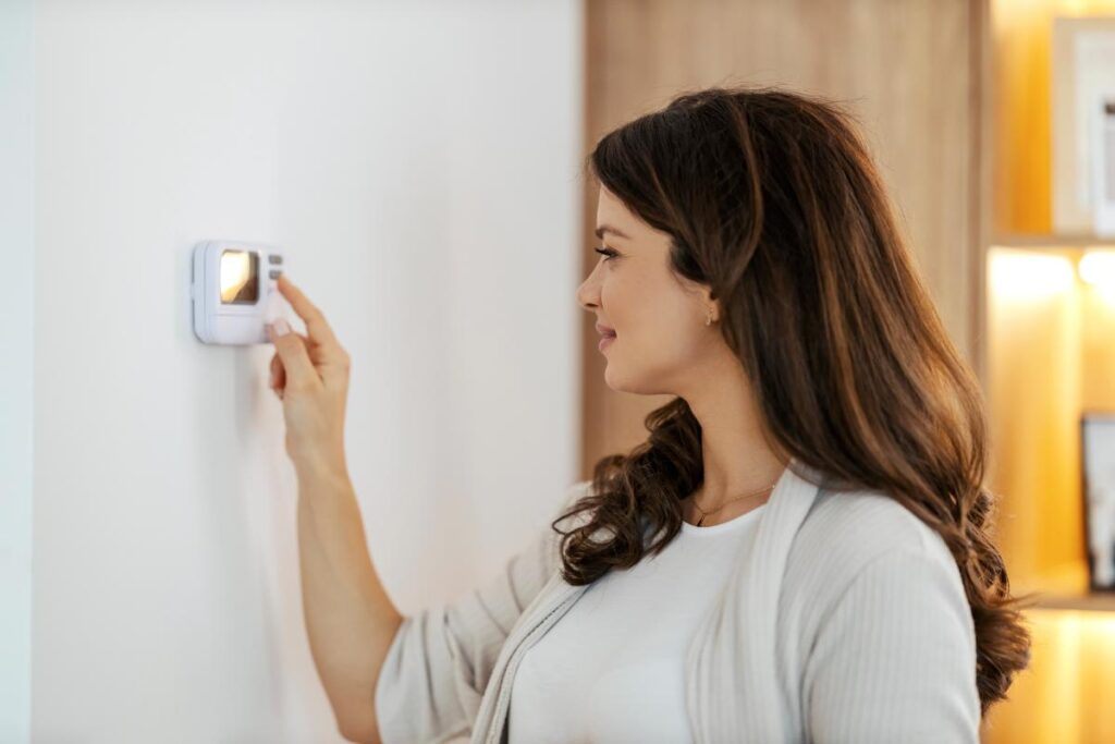a brunette woman adjusting the thermostat in her home