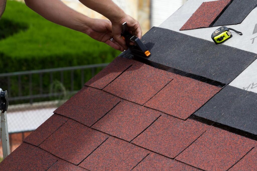 Roofing professional installing red asphalt shingles on a residential roof as part of routine roof replacement and seasonal upkeep.