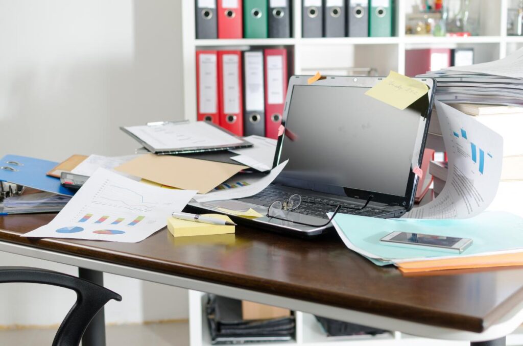 Messy home office desk covered with papers, binders, and a laptop, creating a cluttered space that can attract pests.