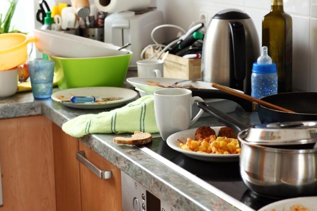 Kitchen counter piled with dirty dishes, cups, and leftover food, showing how everyday messes provide food sources for pests.