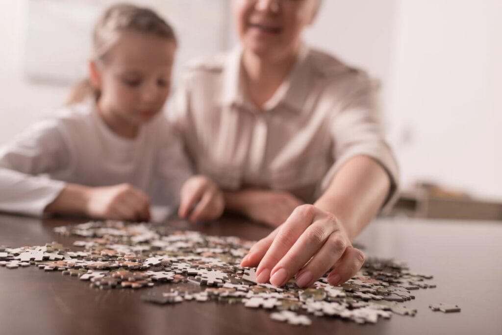 Child and adult working on a jigsaw puzzle together at a table, focused and engaged in a quiet bonding activity.