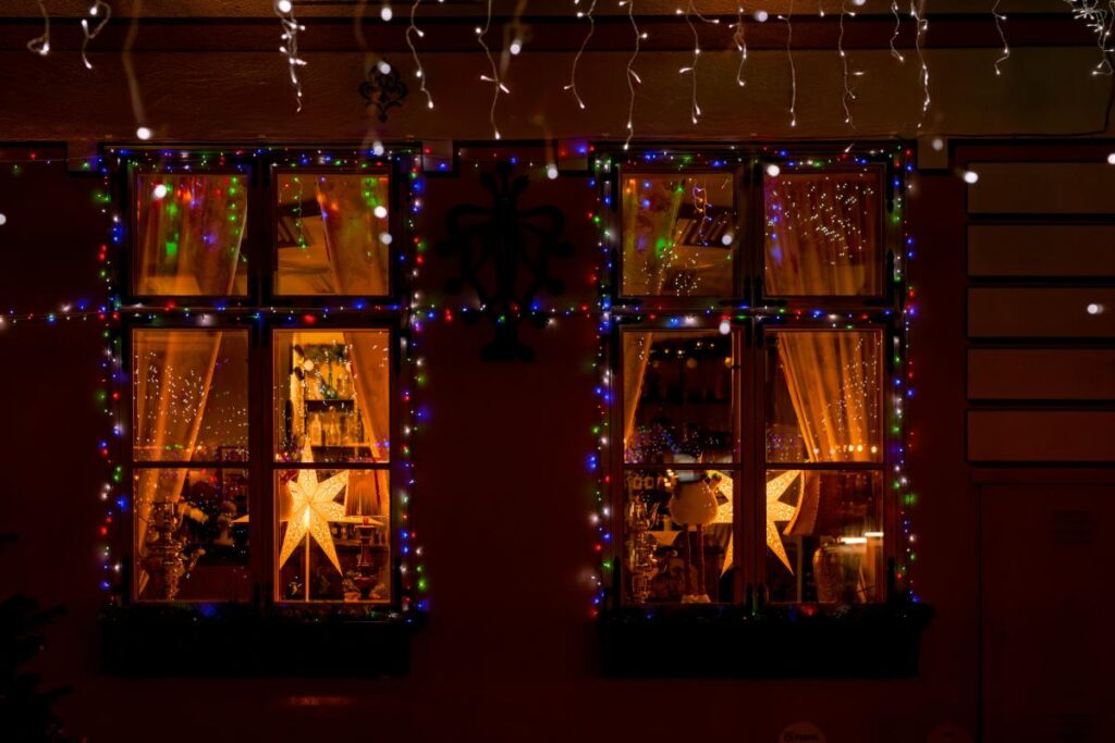 Close-up of festive windows framed with multicolored Christmas lights and glowing star decorations, creating a cozy holiday vibe.