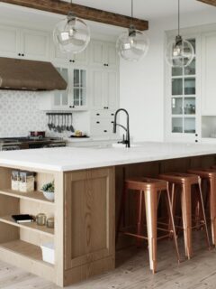 Spacious kitchen remodel featuring a large wood island with a white quartz countertop, copper barstools, pendant lighting, and white shaker cabinets for a functional and stylish coastal design.