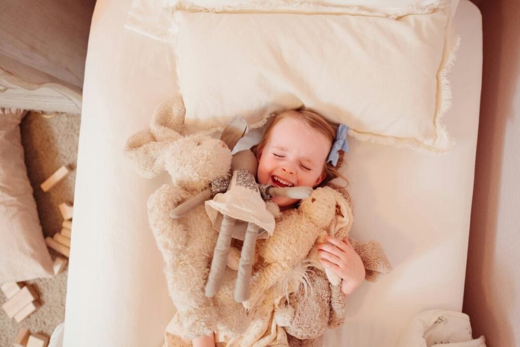young girl laughing and hugging several plush toys