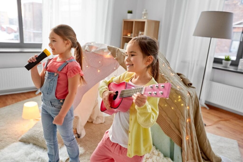Two young girls smiling while singing and playing toy instruments in a cozy room, enjoying creative musical playtime.