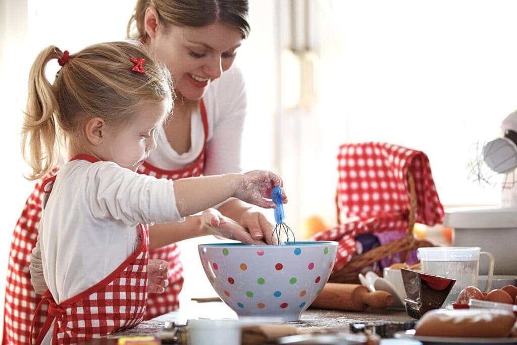 Mother and daughter wearing matching aprons and baking together in the kitchen, mixing batter in a colorful bowl