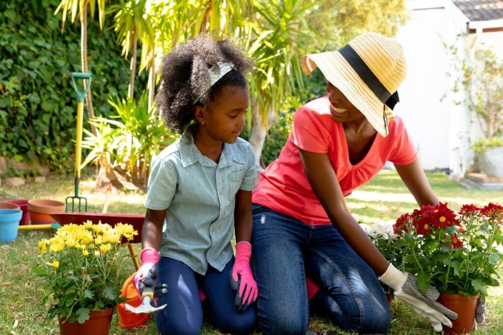 Mother and daughter gardening outdoors, planting colorful flowers together with gloves and tools on a sunny day.