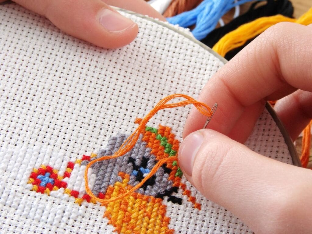 Close-up of hands doing cross-stitch embroidery with colorful thread on fabric, a calm and focused needlework project.