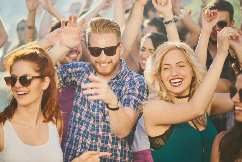 Happy young people dancing and smiling together in the crowd at an outdoor music festival.
