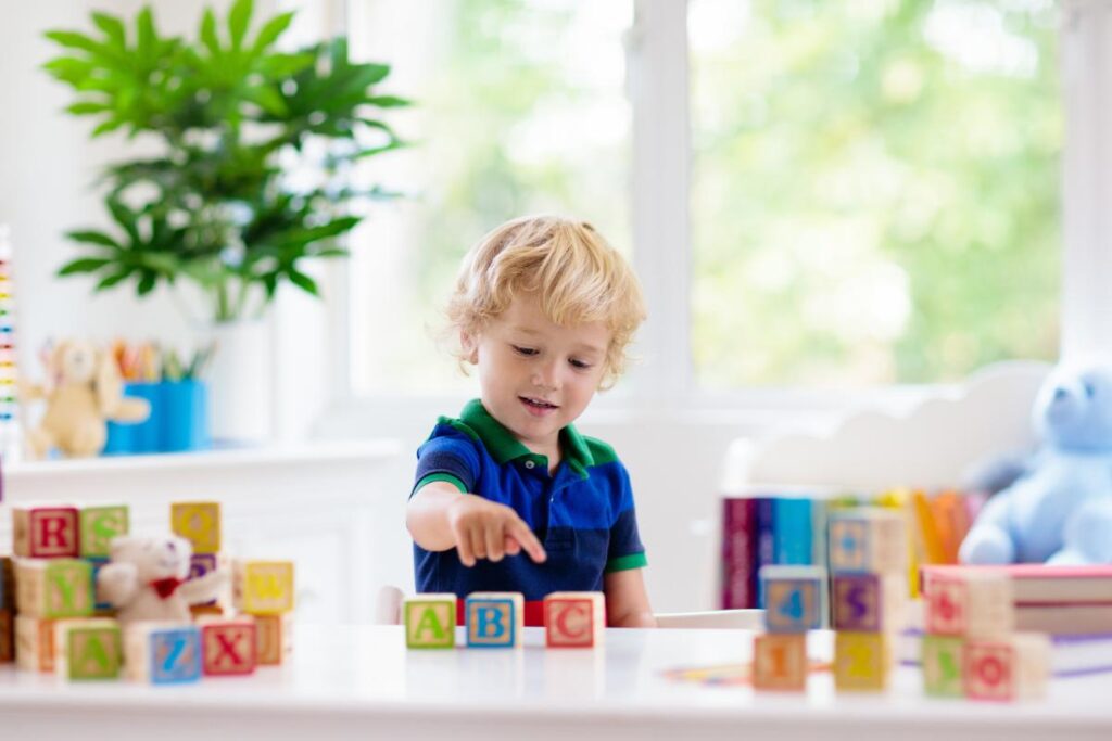 a blond toddler boy with alphabet blocks on a white table