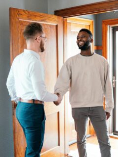 Landlord and tenant shaking hands near the front door of a rental home, symbolizing a positive relationship and successful lease agreement.
