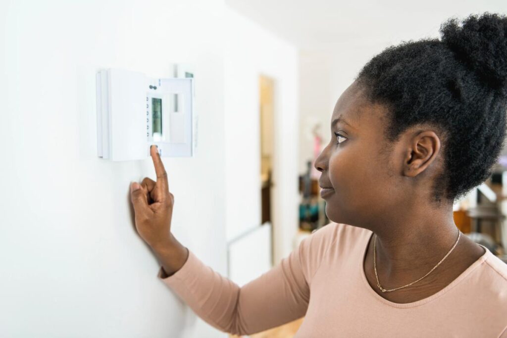 w woman in a pink shirt adjusting the thermostat in her home