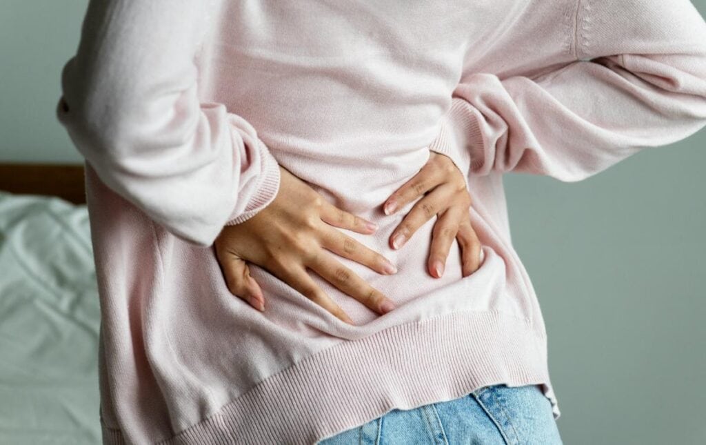 a woman in a pink cardigan holding her lower back because of pain