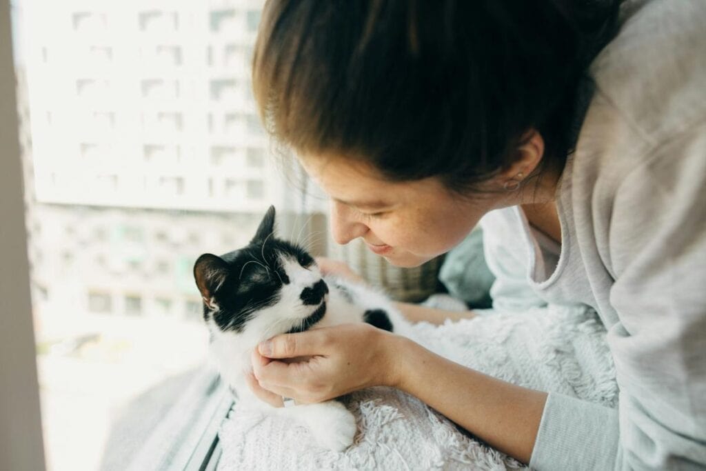 woman lovingly petting her cat near a window