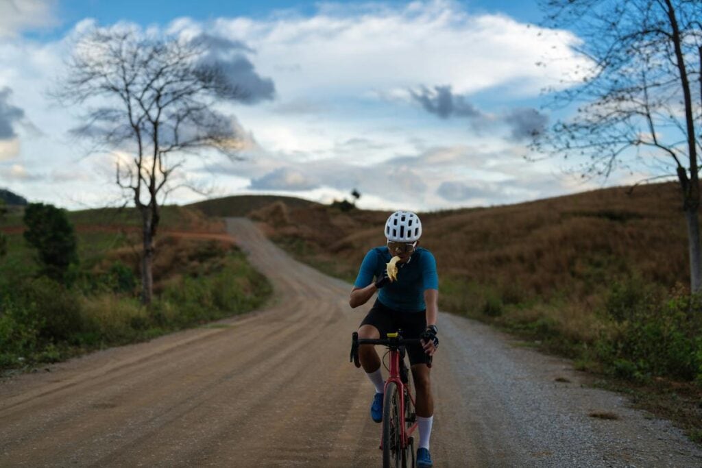 cyclist on a dirt road eating a banana while riding