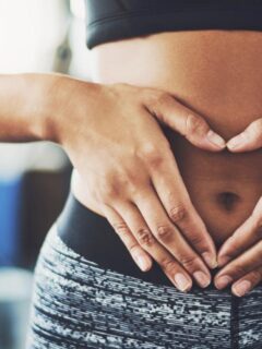 Woman in activewear making a heart shape with her hands over her stomach, symbolising gut health and wellness.