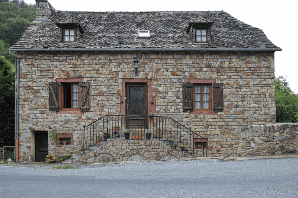 Stone exterior of an old fixer-upper house with rustic wooden shutters and a traditional tiled roof.