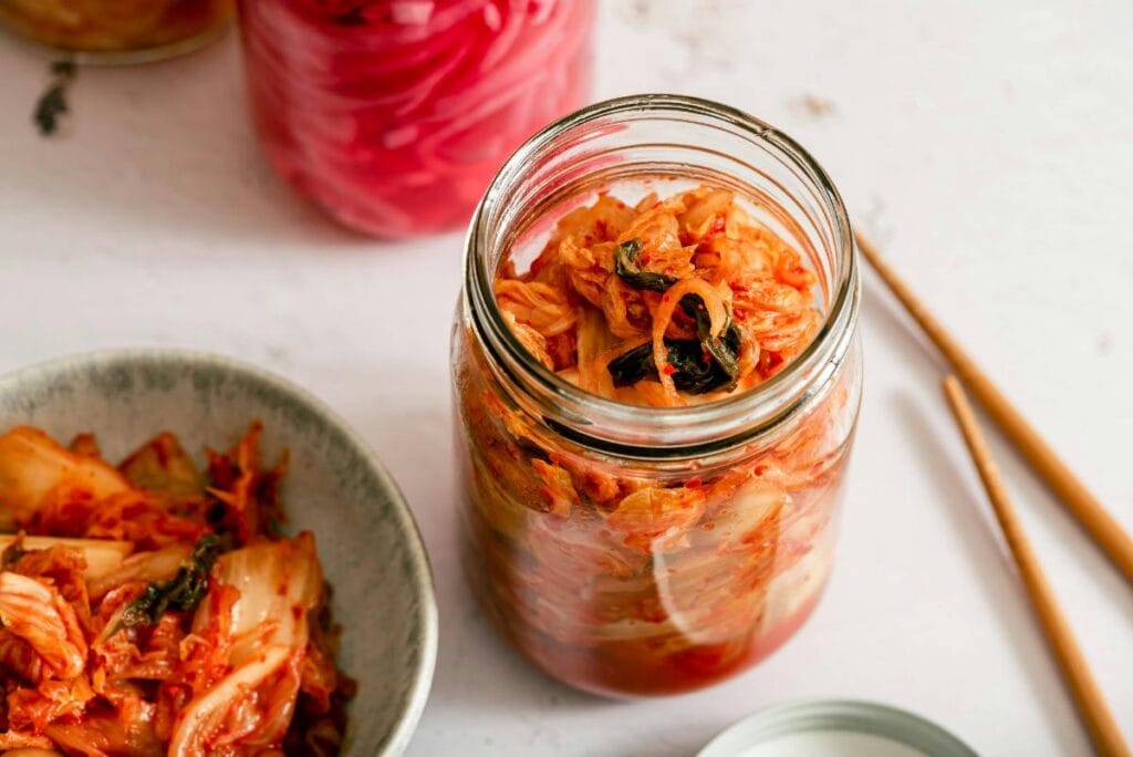 Jar and bowl of kimchi on a light surface, showcasing a probiotic-rich fermented food known to support digestive and gut health.