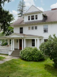 Classic white two-story home with a columned front porch and manicured lawn, showcasing a welcoming and well-maintained exterior entrance.