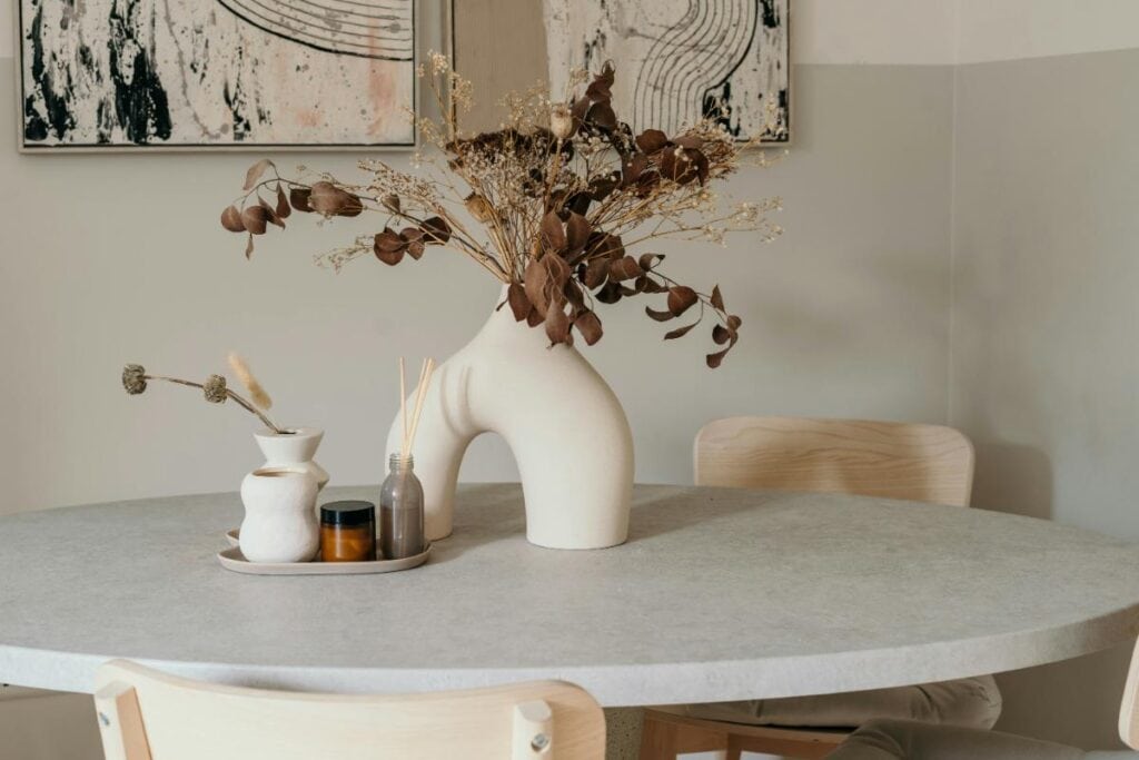 Modern round table with a smooth stone or marble-like surface, styled with sculptural vases and dried floral arrangements in a calm, neutral-toned room.