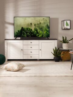 Scandinavian-inspired living room featuring a white TV cabinet with drawers, flat-screen TV, light wood furniture, cozy textiles, and decorative houseplants.