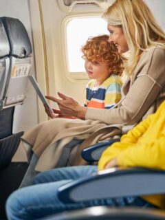 Mother and two children sitting on an airplane, smiling and watching a tablet screen during a flight, enjoying in-flight entertainment.