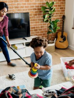 a mom vacuuming the floor while the son and daughter put toys away