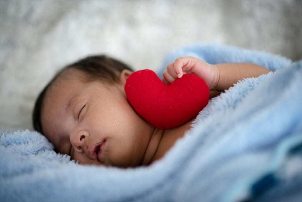 photo of newborn baby with red plush heart