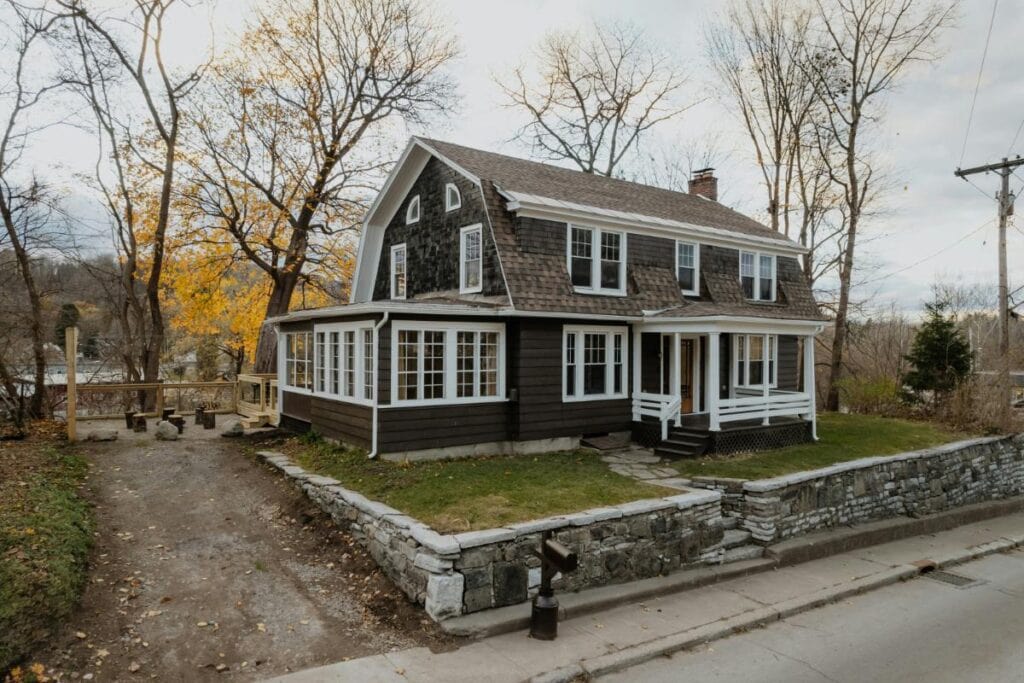 Charming dark brown house with a shingled roof, white trim, and stone retaining wall, highlighting the impact of cohesive design and modern entry features.