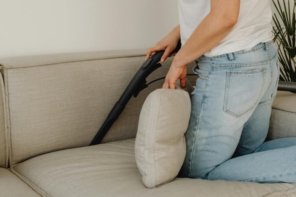 Person vacuuming a sofa cushion to remove dust and allergens for a cleaner, healthier living space.