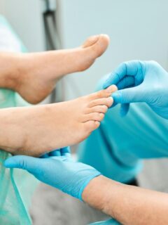 A podiatrist gently inspects a patient’s toes and nails while wearing blue gloves, focusing on detailed foot care in a clinical setting.
