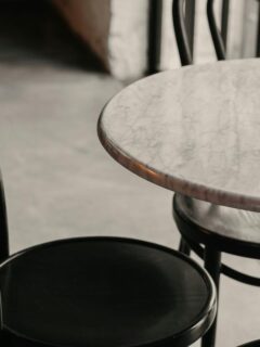 Close-up of a small round marble table paired with black bentwood chairs, set in a stylish, softly lit interior space with industrial elements.