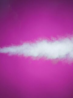 A fog machine emits a stream of white smoke against a vivid pink background, illustrating how controlled effects enhance event ambiance.