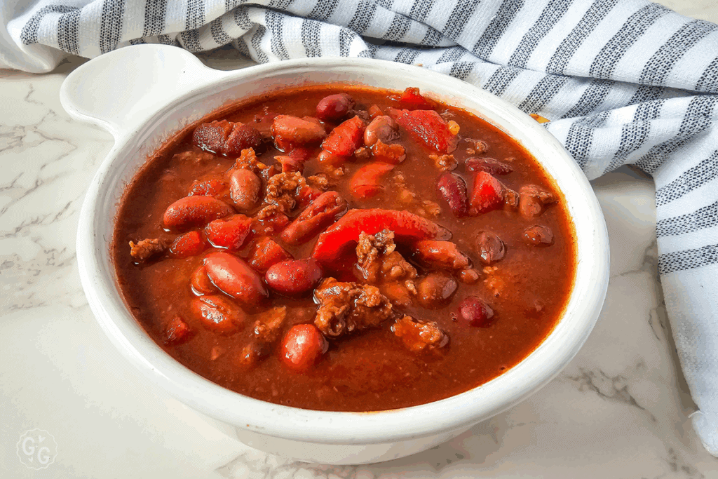 a white bowl filled with venison chili with gray striped dish towel in the background
