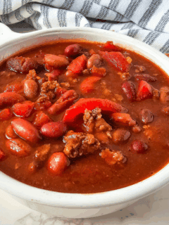 a white bowl filled with venison chili with gray striped dish towel in the background