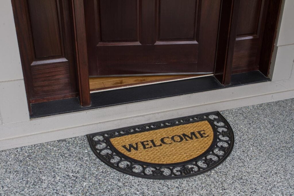 A half-circle doormat with a decorative rubber border and the word "WELCOME" placed at the entrance of a home with a wooden door.