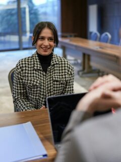A smiling job candidate engages in conversation during an interview, seated across from an interviewer with a laptop in a modern office setting.