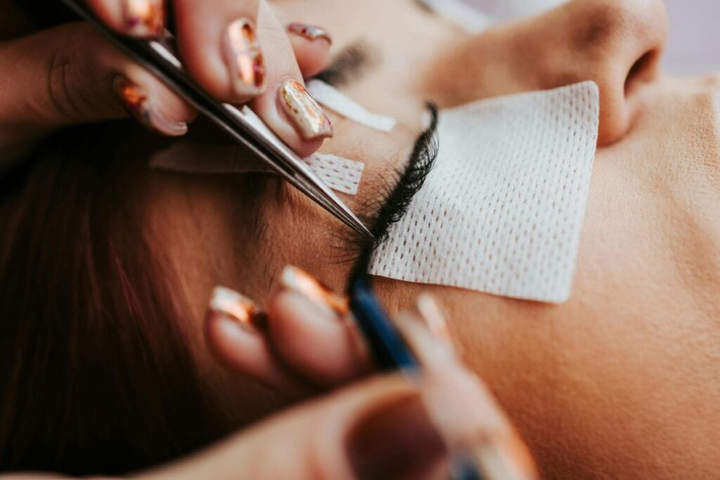 Lash technician applying premade volume fans with tweezers during a professional lash extension session, focusing on precision and technique.