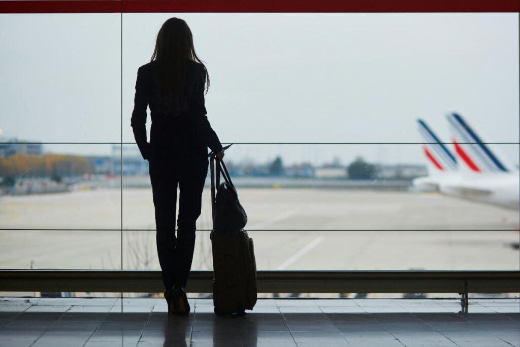 Silhouette of a woman with a suitcase looking out at planes on the runway, capturing the anticipation and planning involved in air travel.