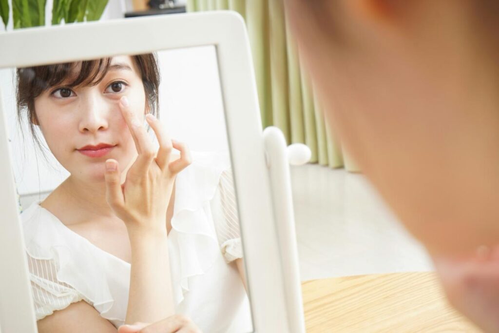 Close-up of a woman applying skincare cream under her eye while looking in a tabletop mirror, highlighting attention to signs of aging.