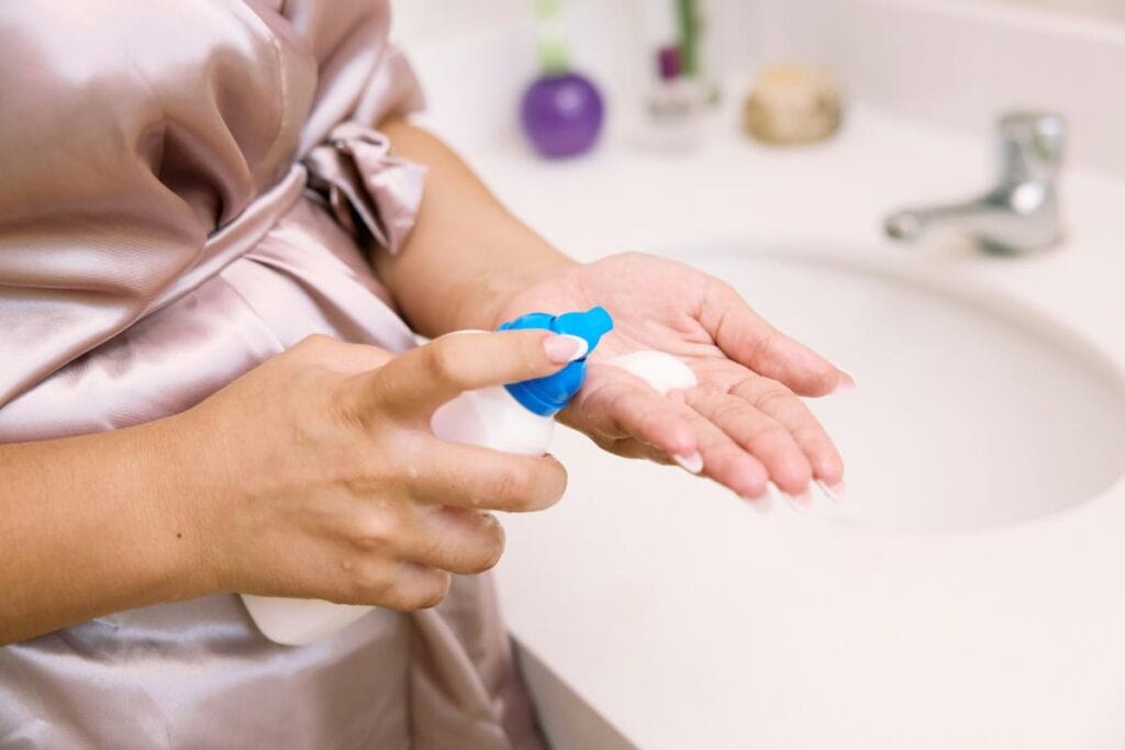a woman pumping facial cleanser into the palm of her hand