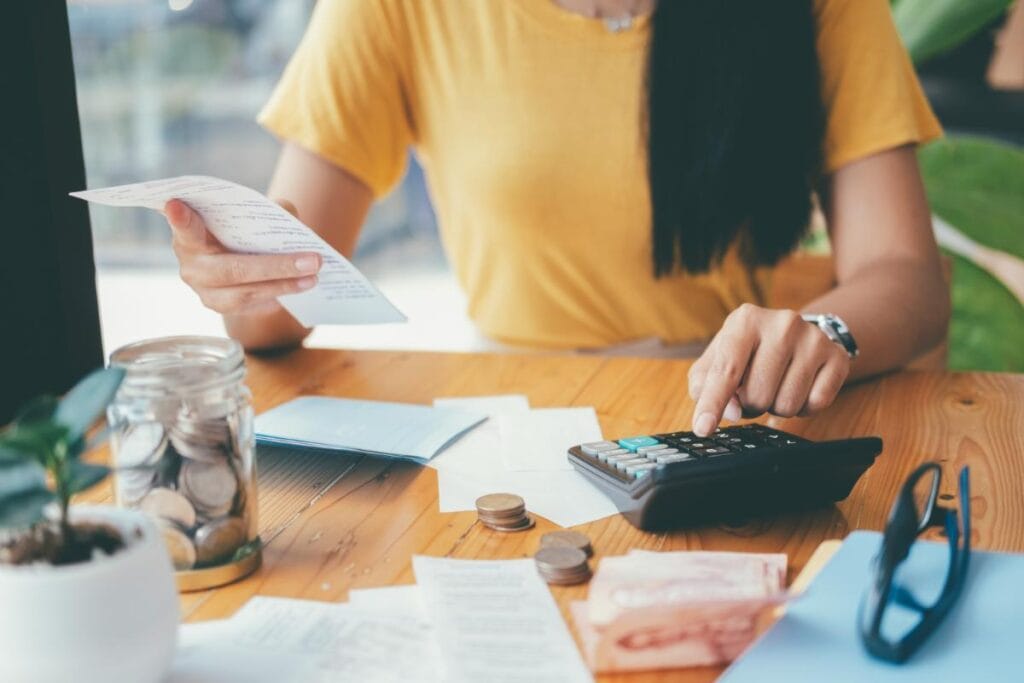woman in a yellow shirt using a calculator while looking at a receipt