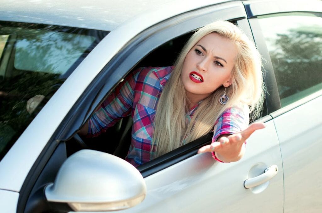 an angry blonde leaning out the car window frustrated with someone in front of her