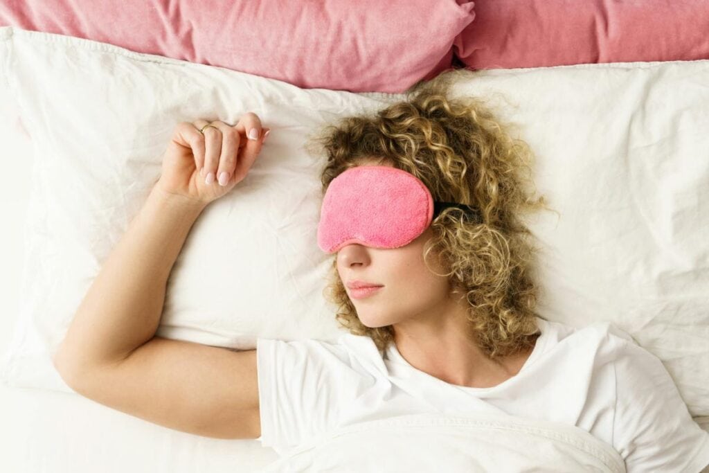 blonde woman with curly hair asleep and wearing a pink eye mask