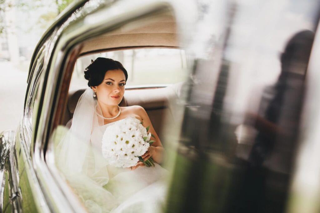 bride with white bouquet sitting in vehicle awaiting transport