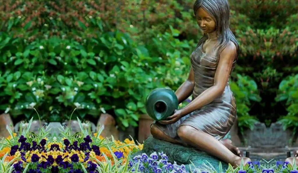 Bronze garden statue with water jug among flowers