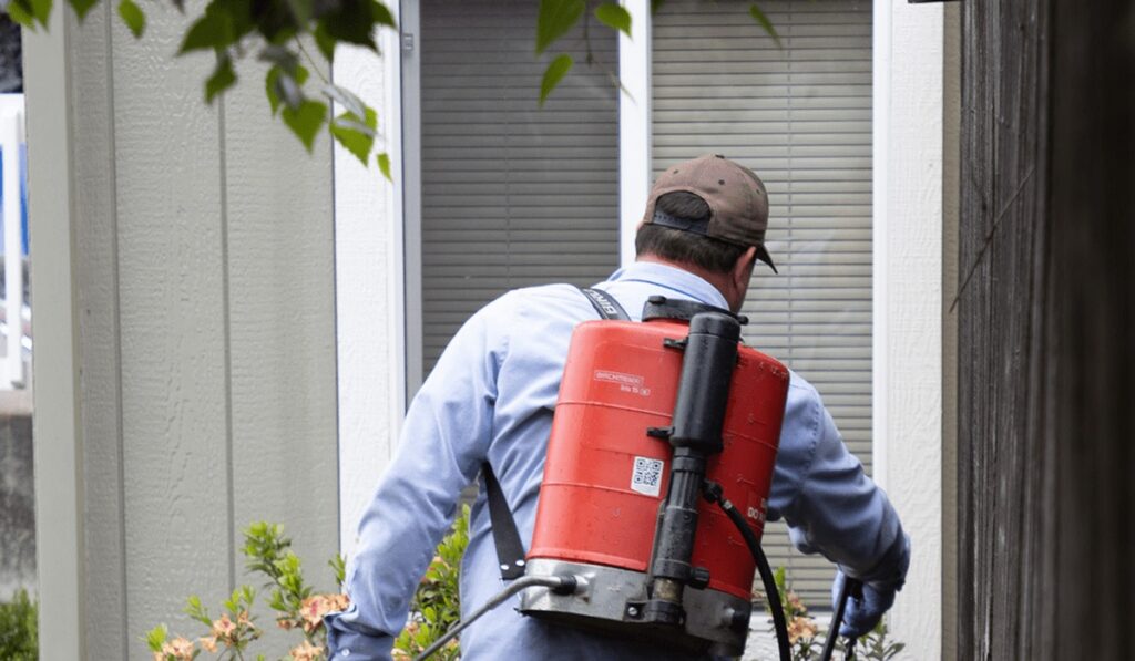 Pest control technician spraying home exterior