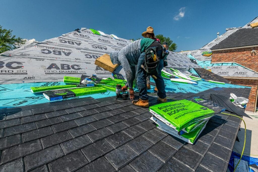 Crew installing shingles on a roof under clear skies, showing proactive roof maintenance to prevent leaks, structural damage, and costly repairs.